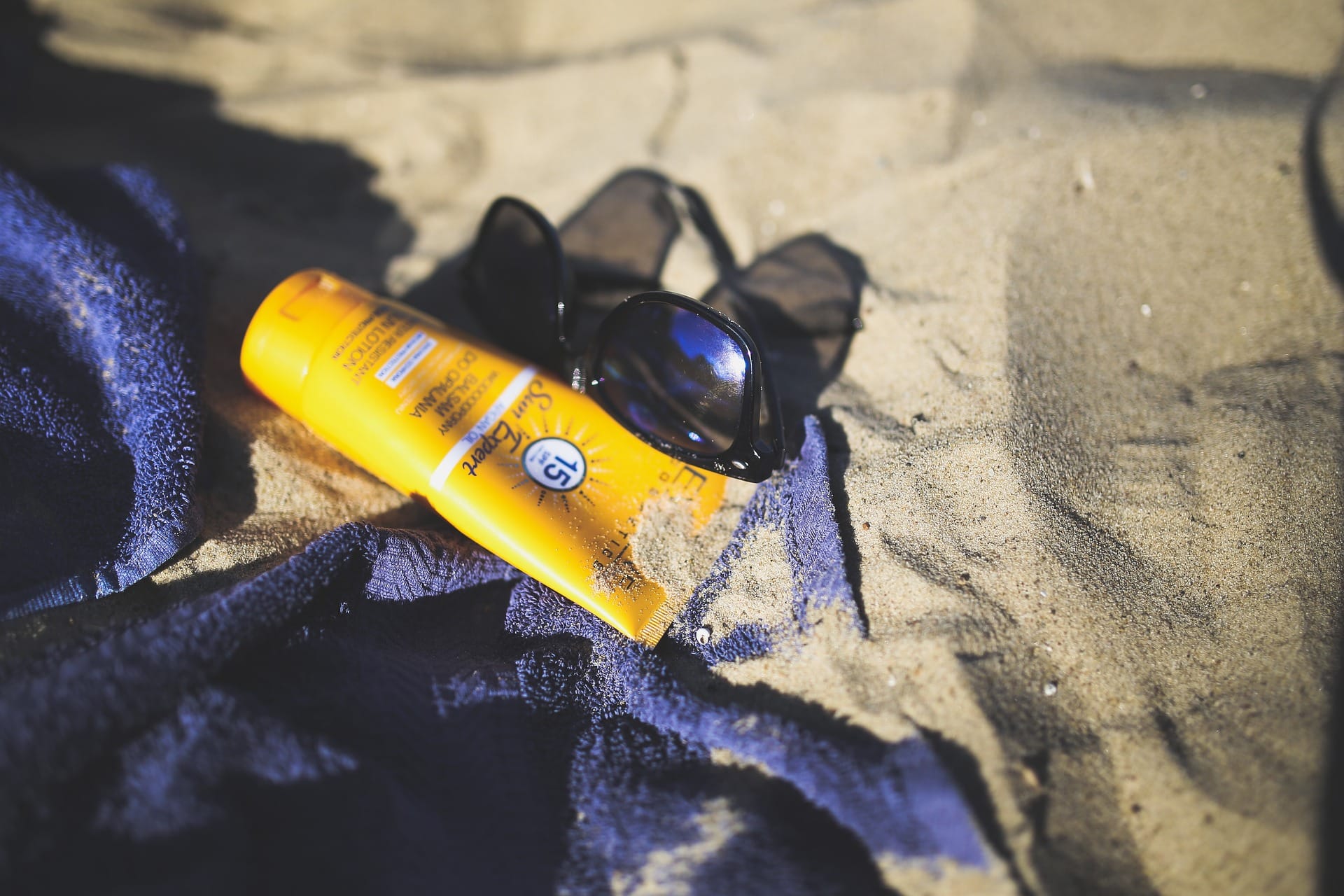 crème solaire sur la plage avec une serviette et des lunettes